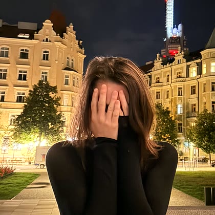 Petra Fišerová sedí večer venku a schovává obličej do dlaní, za ní pražské činžovní domy a televizní věž